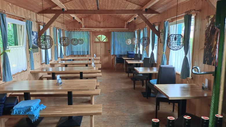 TDR-Zur MUCKE inside, © B.Grohotolszky Interior view of a rustic dining room with wooden tables and benches, decorative lamps and curtains.