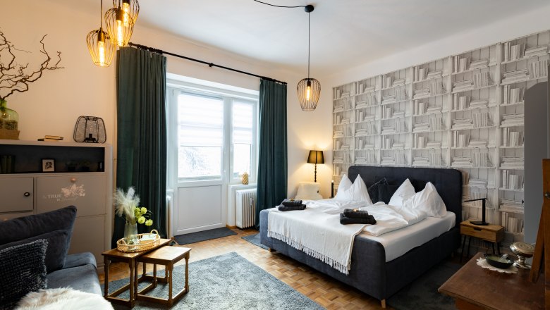 Apartment 1, © Atelier Fürtner-Ton Cozy bedroom with double bed, decorative lamps and bookshelf wallpaper.