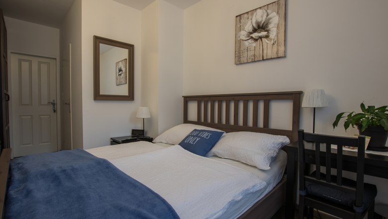 Double room Fuchs, © Dirnbauer Cozy double room with wooden bed, blue ceiling and decorative cushions. A mirror and a flower picture on the wall, next to it a desk with a plant.