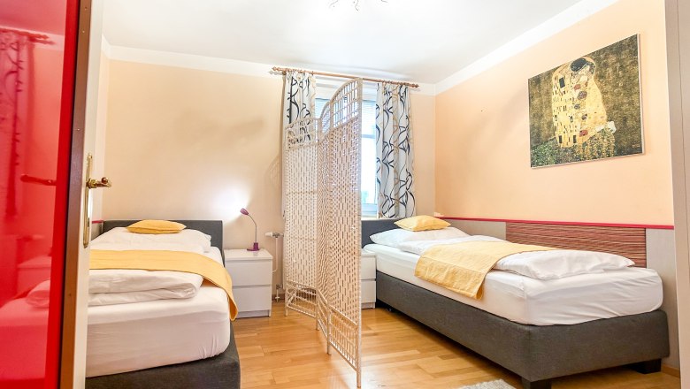 House Morning Sun Bedroom, © Fam. Pauker Bedroom with two single beds, yellow bed linen, a room divider and a painting on the wall.