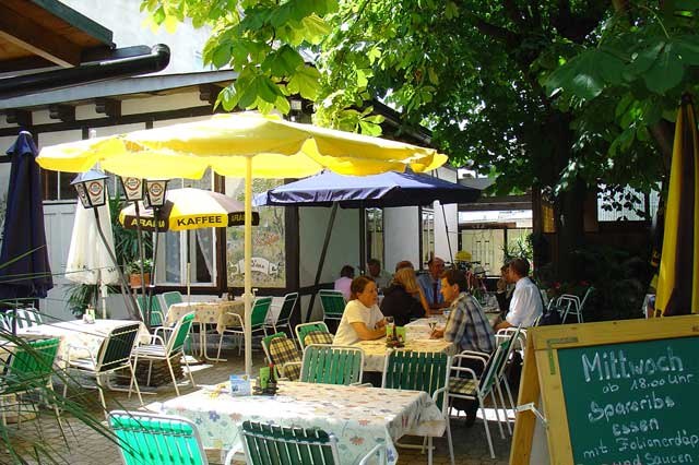 Guest garden, © Gasthof Smrcka A cozy garden with tables, chairs and parasols, surrounded by trees. People are sitting and chatting.