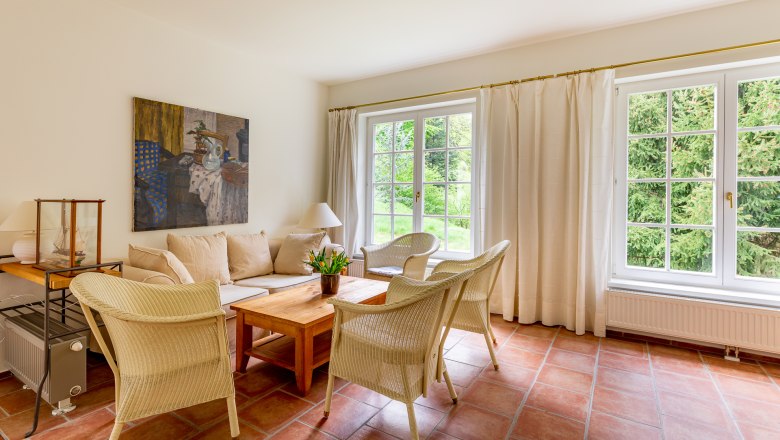 Living space, © Wiener Alpen / Christian Kremsl Bright living room with sofa, wicker chairs, wooden table and large windows with a view of the greenery.