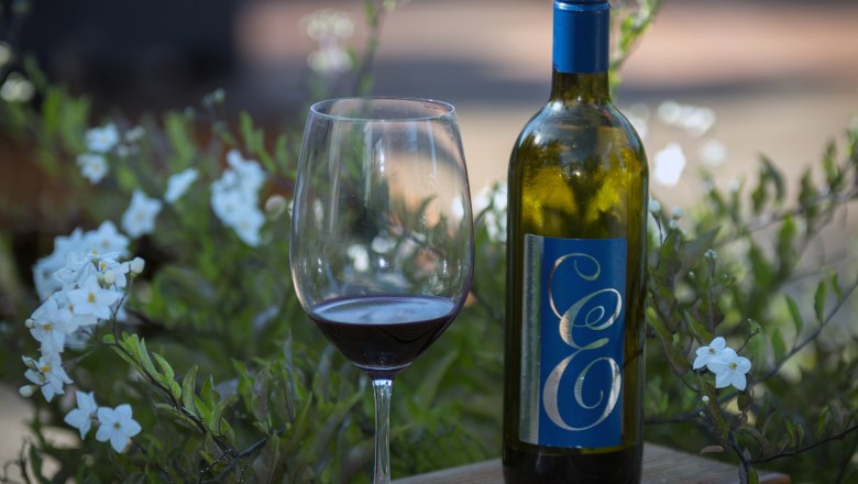Wine from the Edenhof Winery, © Leopold Pluschkowitz Wine bottle and glass on a wooden table with flowers in the background.
