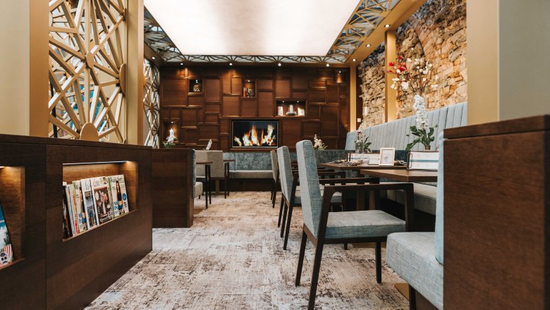 Café living room, © FMS Steinertor Gastronomie BetriebsgmbH Interior view of a stylish café with cozy seating, fireplace and magazine rack.