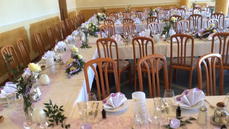 Celebrations at the Kirchenwirt, © Fam. Auer GMBH Festively laid hall with long tables, decorated with flowers and folded napkins.