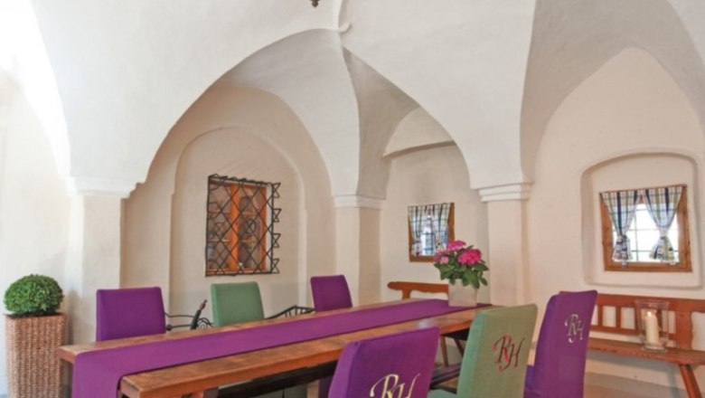 Renaissance Hotel Raffelsberger Hof, © Renaissancehotel “ Raffelsberger Hof “ Interior view of a room in the Renaissance Hotel Raffelsberger Hof with vaulted ceiling, wooden table and chairs with purple and green upholstery.