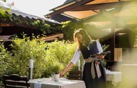 Garden at Landgasthaus Essl, © Inge Funke A woman in traditional dress prepares a table in the garden of a country inn.