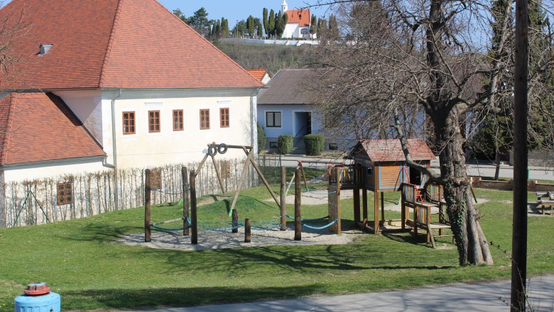 Children's playground at the vicarage, © Souveräner Malteser-Ritter-Orden / Udo Schwamberger A children's playground with a climbing frame and swings next to a building with a red roof.