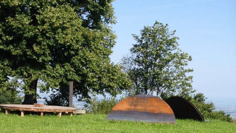 Around show, © Mostviertel Tourismus Wooden platform and metal sculptures on a meadow with trees in the background.