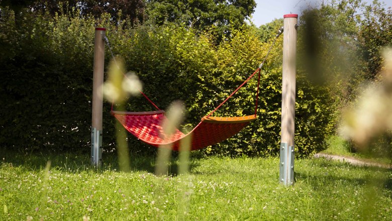 Adventure playground in Joching, © Donau NÖ Tourismus_Barbara Elser Red hammock on a playground surrounded by green vegetation.