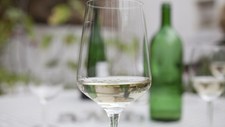 Wine glass, © Weinviertel Tourismus / Christine Wurnig A wine glass with white wine on a table, a green wine bottle in the background.