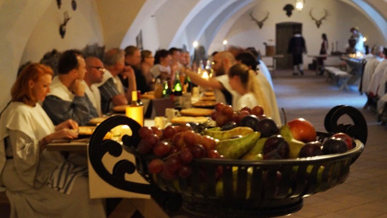 Knights' dinner at Rosenburg Castle, © Schlossschenke People at a knight's dinner in a vaulted hall with a bowl of fruit in the foreground.