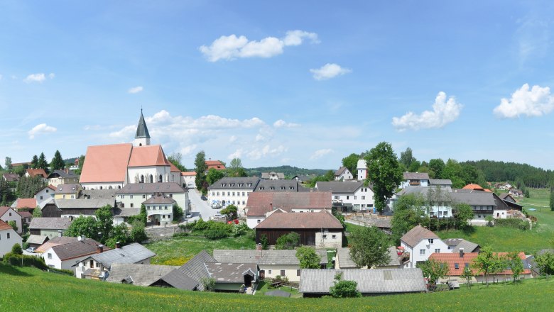 Market town of Schönbach, © Marktgemeinde Schönbach Panorama of the market town of Schönbach with church and surrounding houses, surrounded by green meadows and forests under a blue sky.