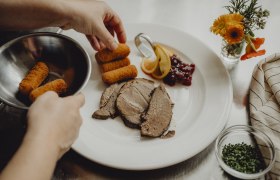 Pub cuisine with specialty weeks, © Niederösterreich Werbung/Rita Newman A plate with meat, croquettes, cranberries and lemon slices is served.