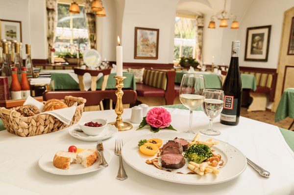 Kirchenwirt, © Best of Wachau_Rita Newman Elegant restaurant with laid table, candle, bottle of wine and plate with meat dish.