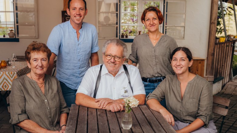 Anton, Cäcilia, Kerstin & Markus Bürgmayr-Posseth, Bernadette Fellner, © Niederösterreich Werbung/Daniela Führer Five people sit and stand around a wooden table in a covered outdoor area.
