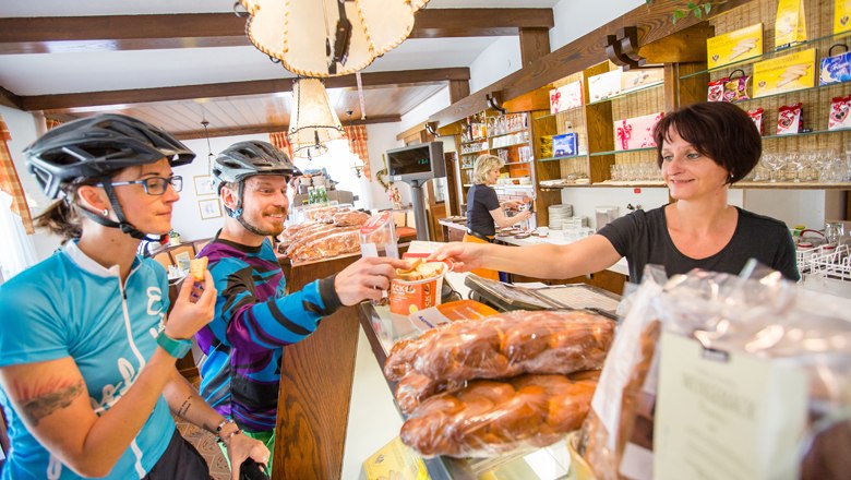 Café Konditorei Alber directly on the Schwarzatal cycle route, © NÖW - Kikinder Two cyclists in a café being served by a sales clerk.