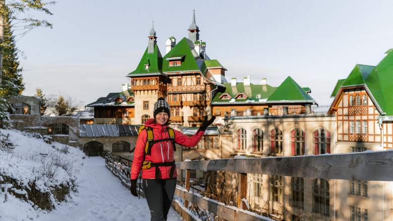 Hiking through villas and palace hotels on the wintry Semmering, © Luxusgämsen Person in winter clothing in front of a large building with green roofs in the snow.