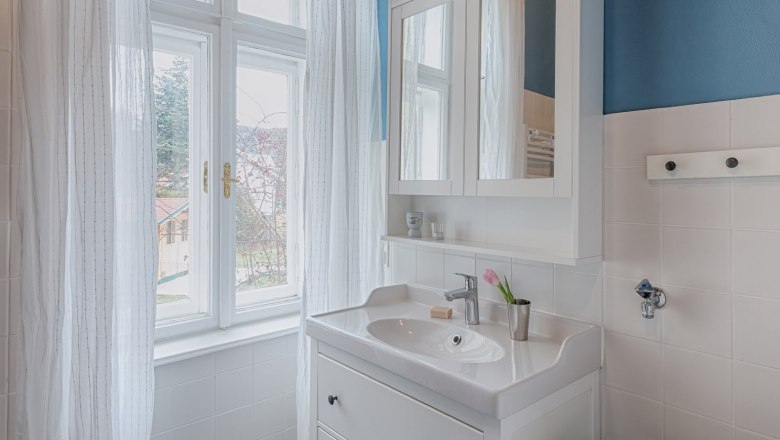Top 2 - Bathroom, © VP FeWo OG Bright bathroom with blue and white tiles, white washbasin and window with white curtains.