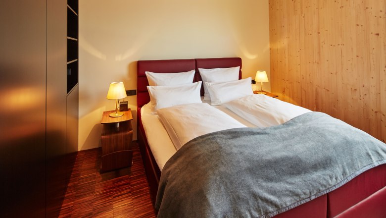 Bedroom in the Guntrams garden loft, © Herbert Lehmann A cozy bedroom with a double bed, red headboard, two bedside tables with lamps and wooden walls.