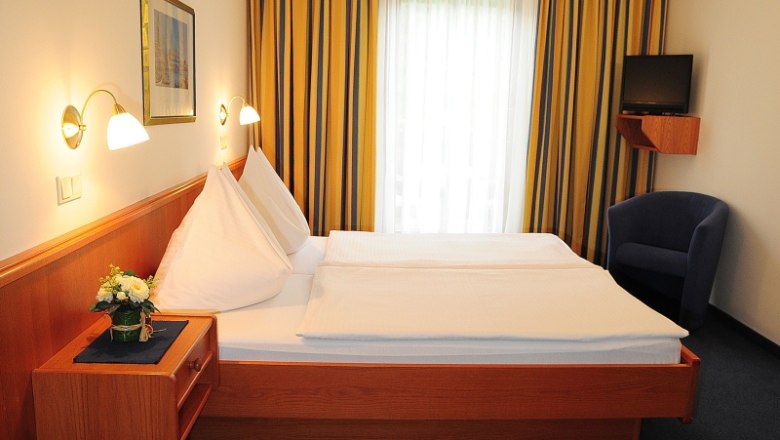 House Oestreicher, © Haus Oestreicher A hotel room with a double bed, blue curtains and a small TV on the wall.