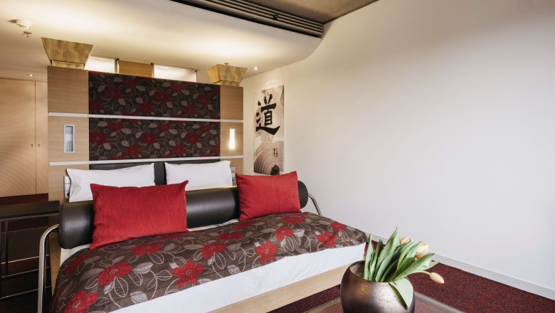 Room Magnolia_Orchid Linsberg Asia, © Linsberg Asia Modern hotel room with double bed, red cushions and floral pattern. A glass coffee table with a vase full of tulips stands in the foreground.