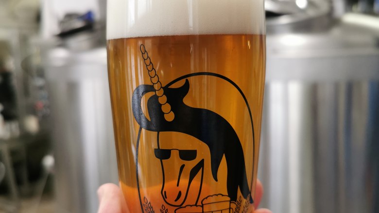 TDR beer glass design, © Drunken Unicorn Beer Factory A beer glass with a unicorn logo and the inscription 'Tradition and Diversity' in front of brewery equipment.