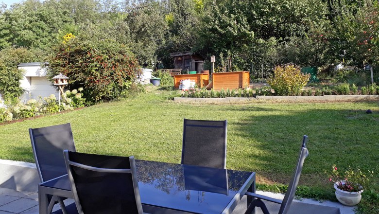 Terrace with garden, © Barbara Muck Terrace with table and chairs, overlooking a garden with lawn, trees and raised beds.