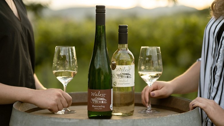 waltz-johann-77, © Weinbau Johann Walzer Two wine bottles and glasses on a wine barrel outdoors.