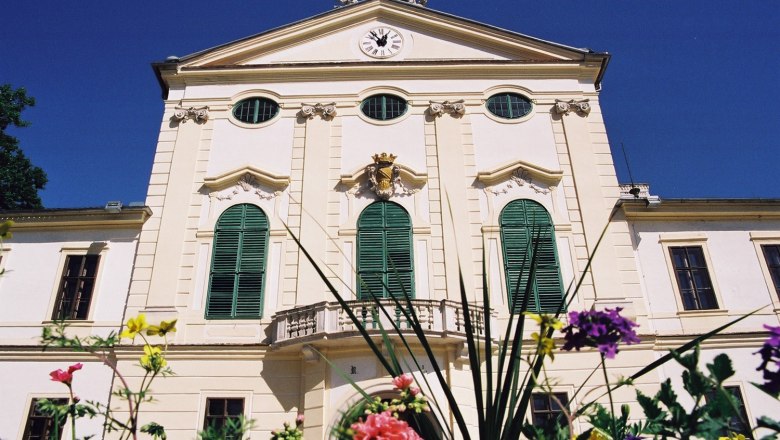 Kirchstetten, © Gemeinde Neudorf/ Staatz Historic building with green shutters and a clock on the façade, surrounded by colorful flowers.
