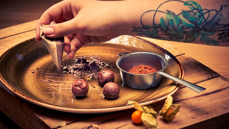 Tavern patisserie, © Niederösterreich Werbung/Andreas Hofer Close-up of a hand with a tattoo decorating chocolate on a plate.