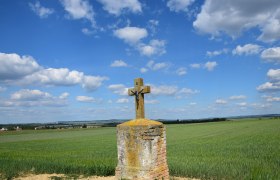 Marterl on Oberer Leite, © Christian Häusler A stone cross with a figure of Christ stands in a field under a blue sky with clouds.