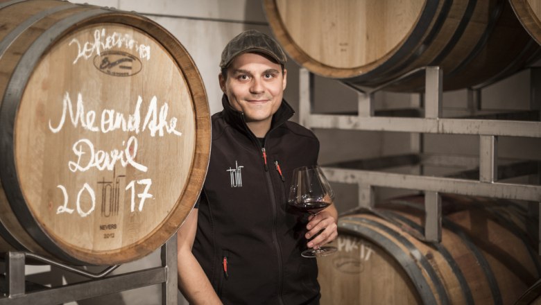 Georg Toifl, © Astrid Bartl Person in wine cellar with wine glass in front of wooden barrels.