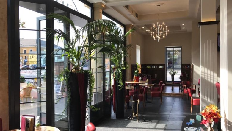 Café Stadler, © Café Stadler Interior view of an elegant café with red chairs, large windows and plants.