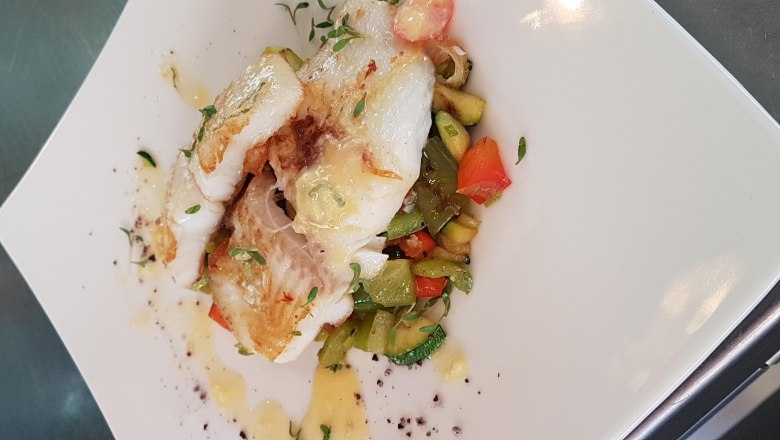 Cod, © Reef & Beef Fried cod on a bed of colorful vegetables, served on a white plate.