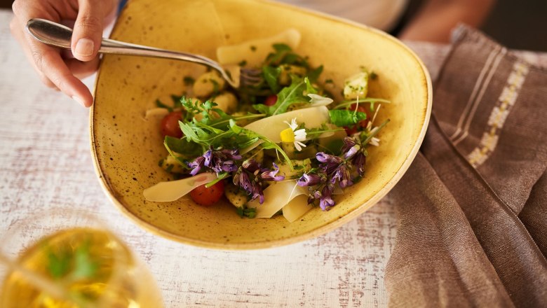 Organic restaurant Leibspeis', © SONNENTOR/ @nudlholz.at A plate with a fresh salad, garnished with edible flowers and rocket, on a table with a glass of drink next to it.