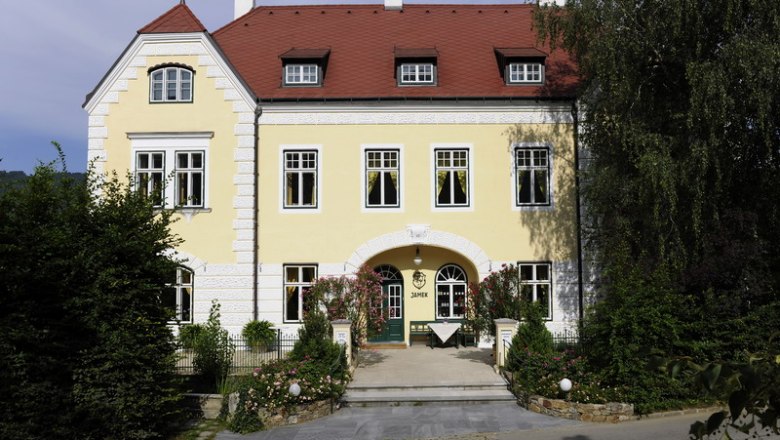 Winery Josef Jamek, © Steve Haider Yellow building with a red roof and green door, surrounded by trees and plants.