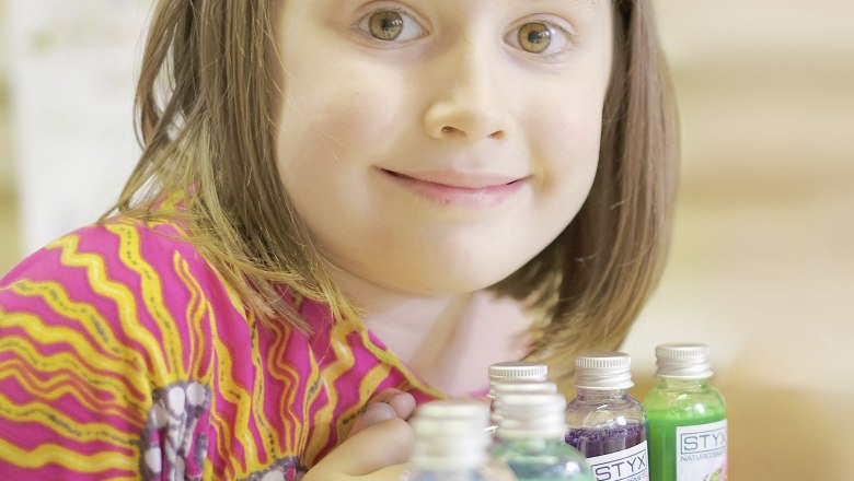 Shower gel workshop, © Styx Naturkosmetic GmbH A child in a colorful top smiles next to small bottles of shower gel.