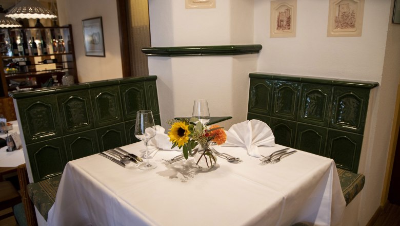 Refreshments and vacation in Baden, © Martinek: Feelimage/Matern Cozy restaurant corner with green tiled stove, table setting and flowers.