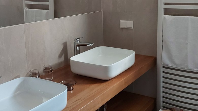 Bathroom, © Bernadette Gierlinger Modern bathroom with two white washbasins on a wooden top, towel rail and basket with towels.