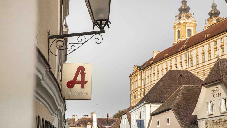 Pharmacy sign in front of the pen, © Landschaftsapotheke Melk Pharmacy sign in front of baroque architecture in a city.