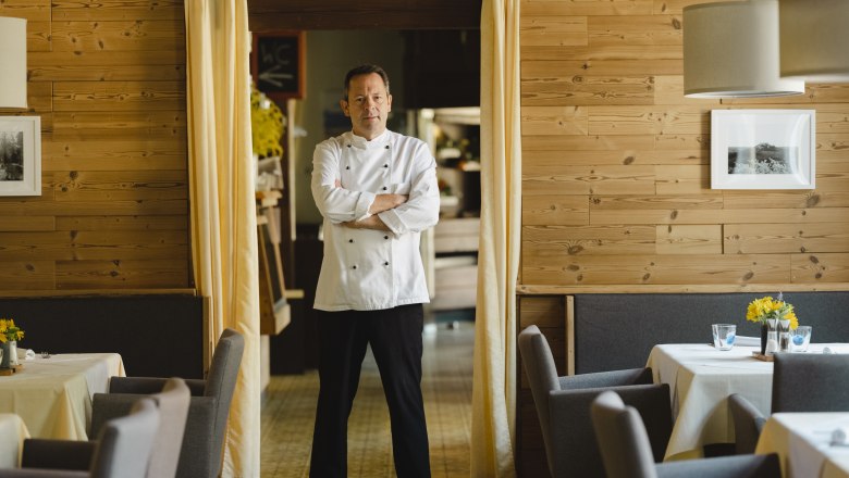 Landlord Martin Weiler, © Niederösterreich Werbung/Michael Reidinger A man in chef's clothes stands with his arms folded in a restaurant with wooden walls.