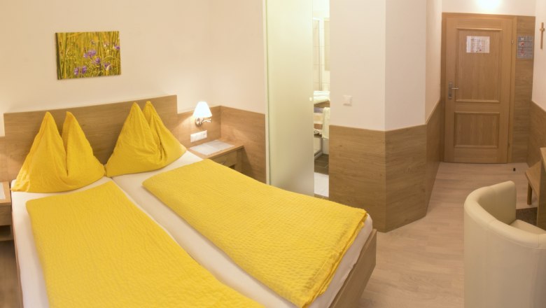 Rooms, Hotel zur Linde, © Ing. Matthias Schön Hotel room with yellow bed linen, wooden furniture and a picture on the wall.