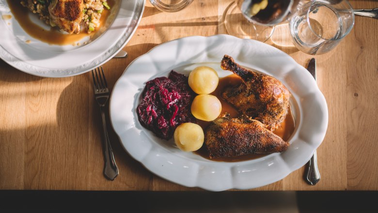 Oven-fresh farm duck, © Niederösterreich Werbung/Mara Hohla A plate of roast duck, red cabbage and potatoes on a wooden table.