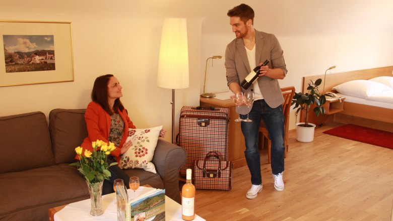 Double room Superior, © Schendl A man pours wine for a woman in a cozy hotel room.