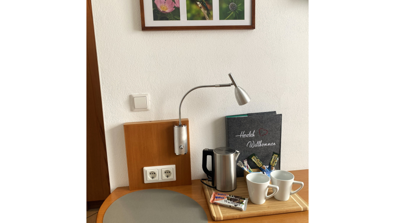 Room, © Trachsler A table with a kettle, two cups, snacks and a welcome booklet. Three nature photos hang on the wall.