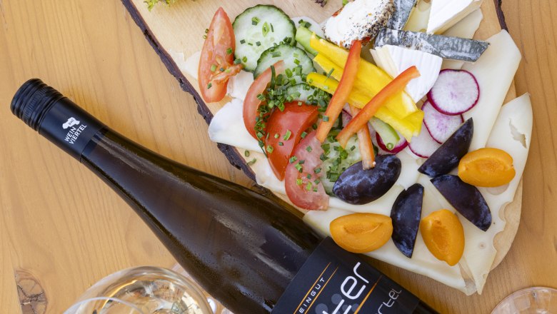Heurigen platter, © Weinviertel Tourismus GmbH / Schwarz-König Heurigen platter with cold cuts, cheese, vegetables and wine on a wooden table.