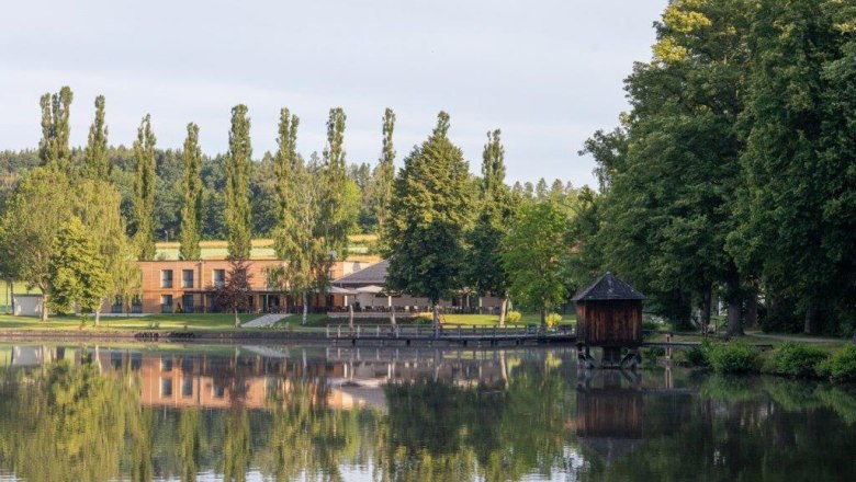 Hotel-Restaurant Hausschachen, © Hotel-Restaurant Hausschachen Lake with shore building and trees, peaceful landscape scene.