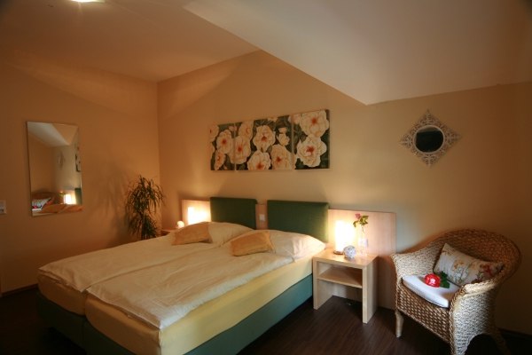 Nostalgia room, © Rosenhotel Cozy bedroom with double bed, rattan armchair, bedside table and flower picture on the wall.