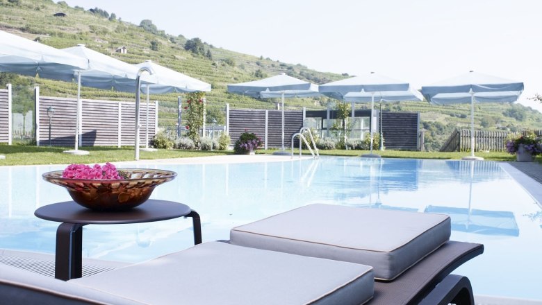 Outdoor pool, © Steigenberger Hotel and Spa An outdoor pool with sun loungers and parasols set against a hilly landscape.
